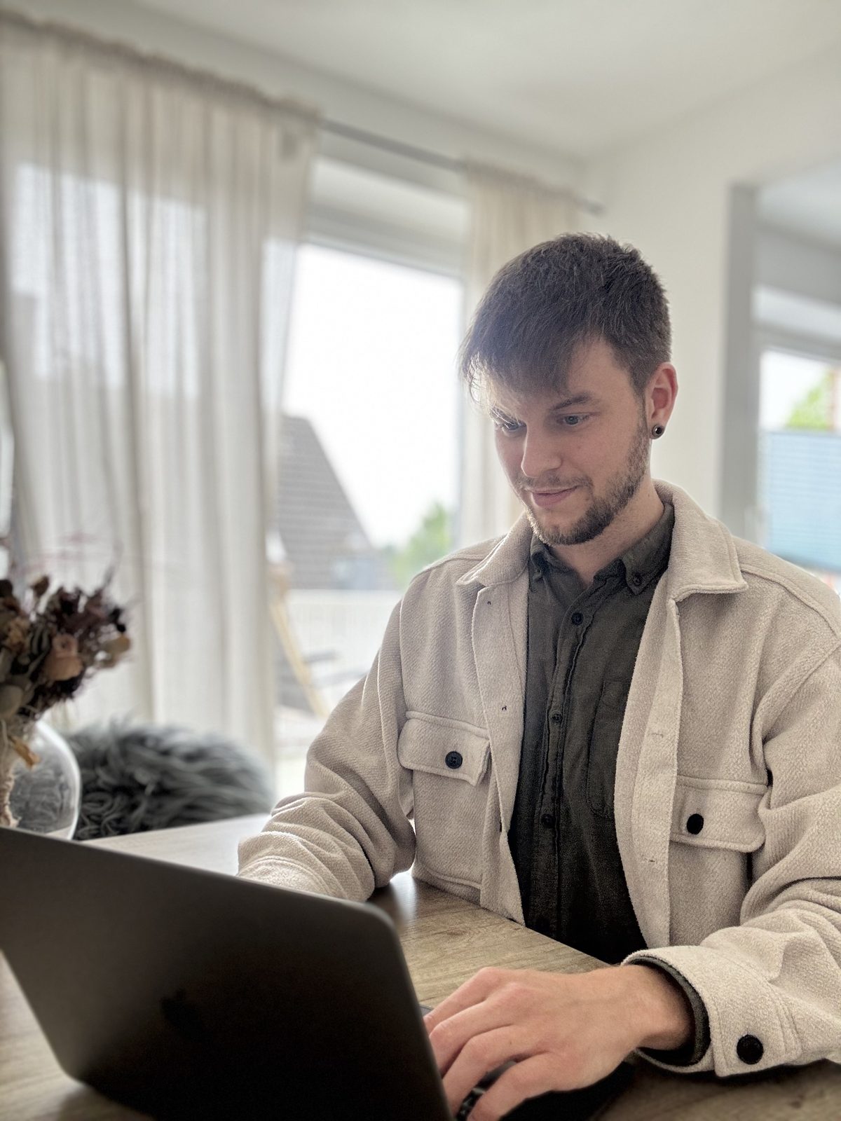 Lukas Babbick arbeitet am Laptop vor einem hellen Fenster